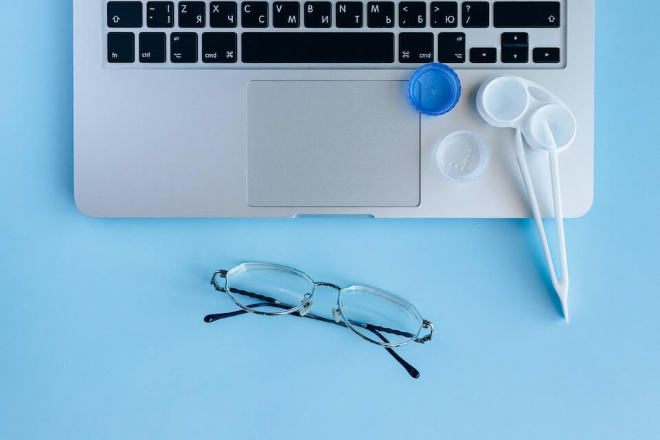 Eyeglasses and contacts next to a Macbook
